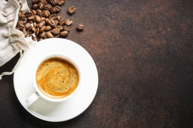 Koyu masada bir fincan kahve ve kavrulmuş kahve çekirdeği. Tasarım için alanı olan üst görünüm.