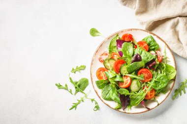 Green salad with fresh leaves and vegetables in white plate. Top view.