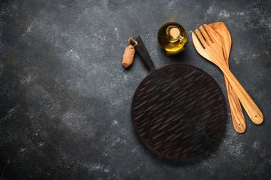 Kesme tahtası, ahşap çatal bıçak ve siyah arka planda yağ şişesi olan mutfak masası. Kopyalama alanı olan üst görünüm.