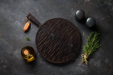 Mutfak aletleri, otlar ve baharatlarla siyah arka planda kesim tahtası. Kopyalama alanı olan üst görünüm.