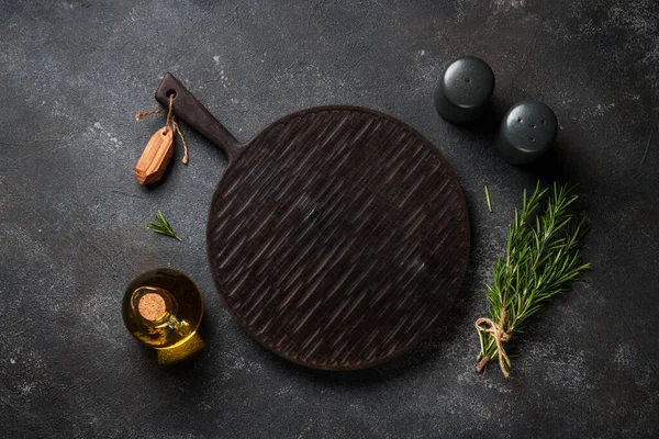 Mutfak aletleri, otlar ve baharatlarla siyah arka planda kesim tahtası. Kopyalama alanı olan üst görünüm.