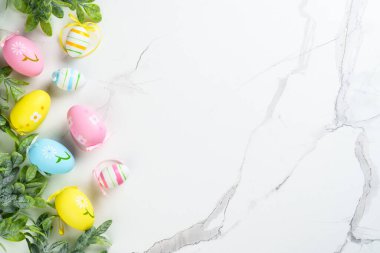 Beyaz arka planda renkli yumurtalar ve yeşil bitkilerle Paskalya kompozisyonu. Kopyalama alanı olan düz.