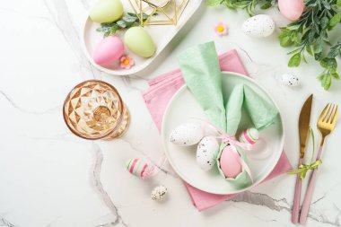 Beyaz arka planda bahar dekorasyonlu Paskalya sofrası. Beyaz tabak, çatal bıçak takımı ve renkli yumurta. Kopyalama alanı olan düz.