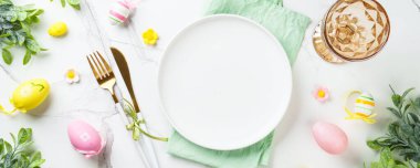 Beyaz arka planda Paskalya sofrası. Beyaz tabak, çatal bıçak takımı ve paskalya süslemeleri. Web pankartı biçimi.