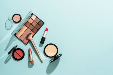 Mavi arka plandaki ürünleri uydur. Kozmetik palet, fırçalar, krem ve ruj. Kopyalama alanı olan düz resim