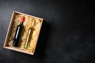 Siyah arka planda kırmızı ve beyaz şarap. Tahta kutuda iki şişe. Kopyalama alanı olan üst görünüm.