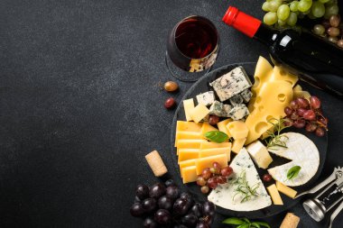 Peynir tabağı ve kırmızı şarap. Kaykay tahtasındaki üzümlü el yapımı peynir. Siyah arkaplanda üst görünüm.