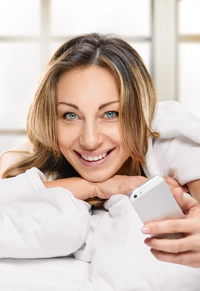 Mujer radiante con teléfono acostado en la cama — Foto de Stock