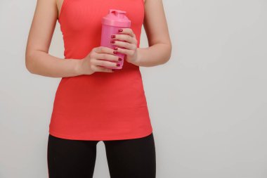 Spor giysilerinde kadın fitness modeli gri arka planda su şişesiyle poz veriyor.