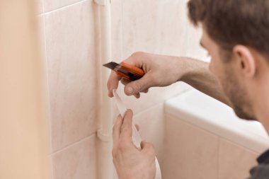 Banyodaki boruya yapışkan bant yapıştıran adama yaklaş.