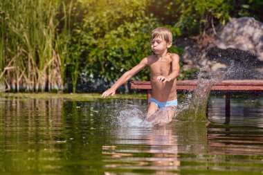 Küçük çocuk eğleniyor ve iskeleden nehre atlıyor.