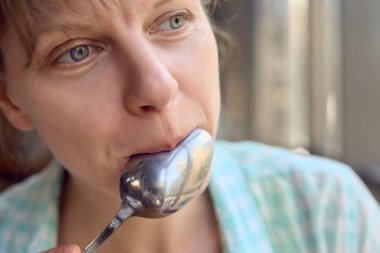 Lezzetli yemeklerden sonra kaşığı yalayan genç kadının yakın plan portresi.