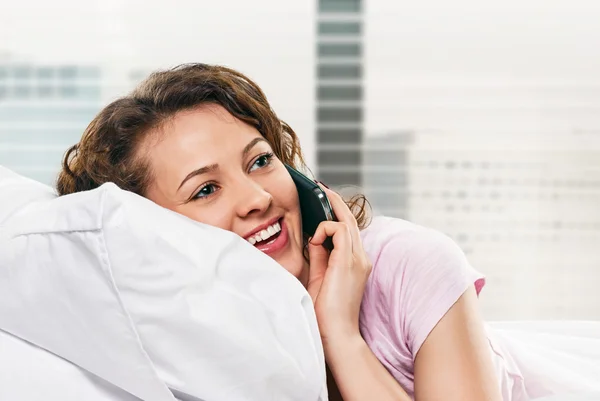 Strahlende Frau mit Handy im Bett liegend — Stockfoto