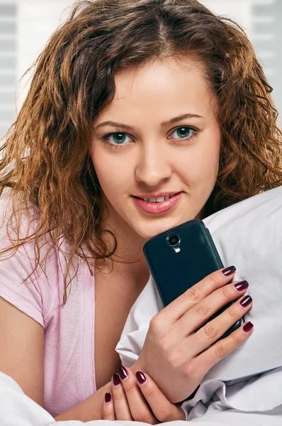 Parlak kadın yatakta yatarken telefon ile — Stok fotoğraf