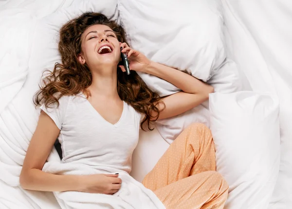 Stralende vrouw met telefoon liggend op bed — Stockfoto