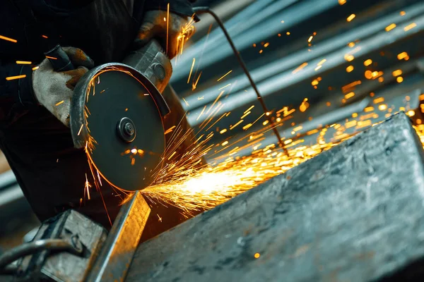 Cutting a metal beam using an angle grinder. A lot of sparks fly out from under the disk