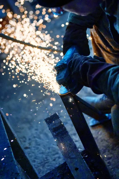 Cutting a metal beam using an angle grinder. A lot of sparks fly out from under the disk