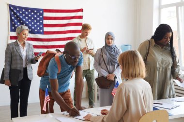 Seçim günü Amerikan bayraklarıyla süslenmiş sandık merkezinde kayıt yaptıran çok ırklı geniş bir grup.
