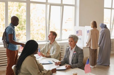 Amerikan bayraklarıyla süslenmiş sandık merkezinde oy veren çok ırklı bir grup insanın geniş açı görüşü, kopyalama alanı
