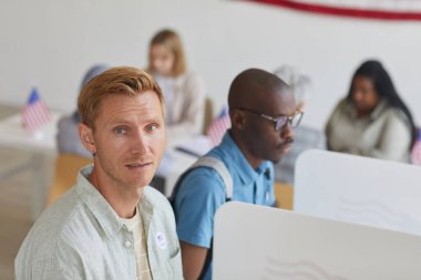 Seçim günü oy verme kabininde dikilirken kameraya bakan modern sarışın adamın yüksek açılı portresi, boşluğu kopyala