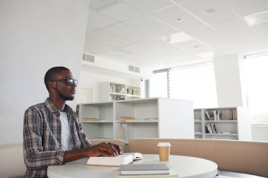 Kör Afro-Amerikan bir adamın kütüphanede Braille kitabı okuyup, kopyaladığı yan görüntü portresi.