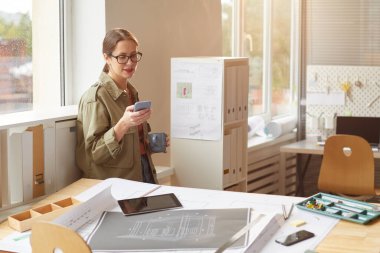 Kahve içen ve kahve molası sırasında akıllı telefon ekranına bakan genç bir kadının sıcacık tonlu portresi.