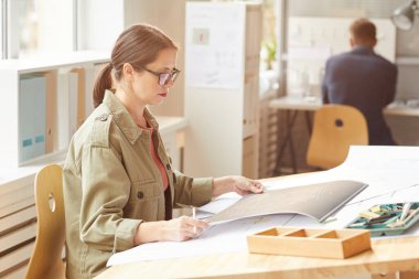 Güneş ışığında çizim masasında otururken planlara bakan genç bayan mimarın yan görünüm portresi, boşluğu kopyala