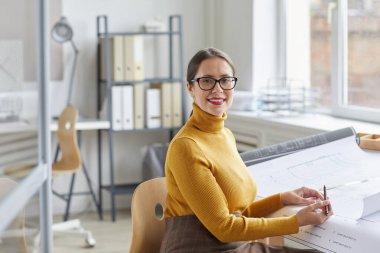 Ofiste masa başında oturmuş kameraya bakan gülümseyen kadın mimarın portresi, boşluğu kopyala