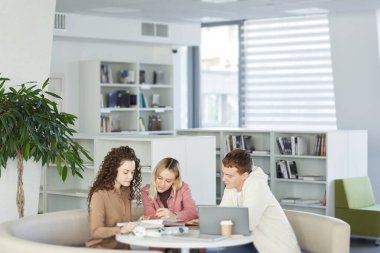 Üniversite kütüphanesinde masada oturup grup projesi üzerinde çalışırken birlikte çalışan üç gencin portresi, boşluğu kopyala