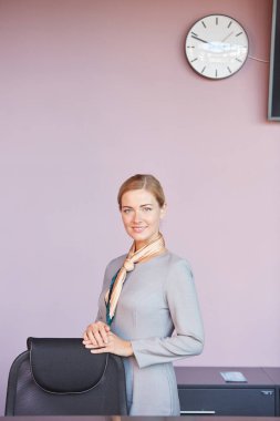 Ofiste mor duvara yaslanırken kameraya bakan zarif genç kadının dikey portresi, boşluğu kopyala