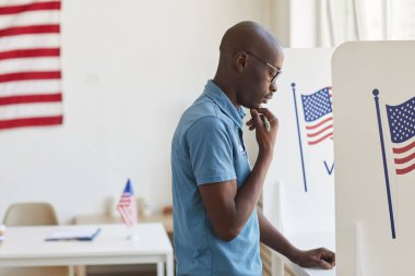 Oy verme kabininde duran ve uzayın fotokopisini çekmeyi düşünen Afro-Amerikan bir adamın yan görüntüsü.