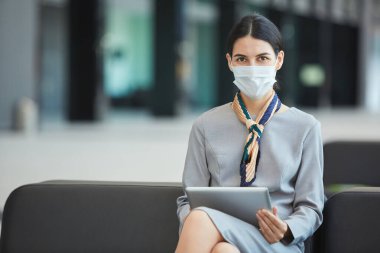 Maske takan kadın hostes portresi ve bekleme salonundaki kanepede oturmuş kameraya bakarken,