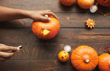 Yukarıdan bakıldığında, Cadılar Bayramı partisi için olgun balkabağını oyan elleri, koyu kahverengi ahşap masa üzerinde mutfak bıçağıyla yatay olarak gösteren bir görüntü.