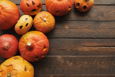 Cadılar Bayramı için oyulmuş olgun turuncu balkabaklarından oluşan düz bir kare. Kahverengi ahşap masa üzerinde duruyor. Boşluğu kopyala.