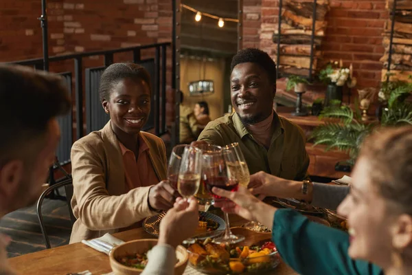 一对年轻的非洲裔美国人夫妇在舒适的室内与朋友和家人共进晚餐时碰杯的肖像 — 图库照片