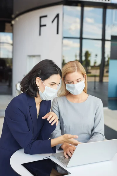 两个成功的女商人头戴口罩站在写字台前看笔记本电脑屏幕时的竖直腰高肖像 — 图库照片