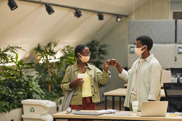 Portrait of two young African-American people bumping fists as contactless greeting while working in post pandemic office, copy space