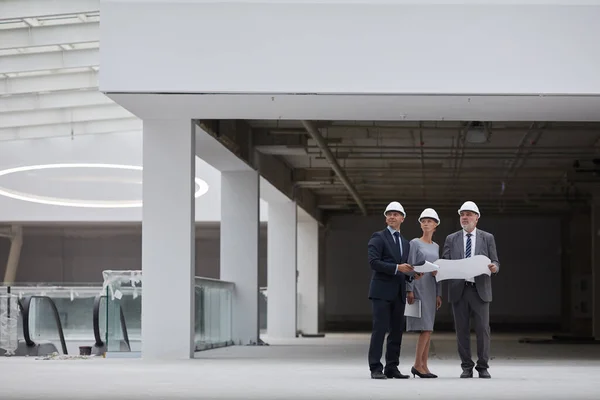 三位成功的商人戴着安全帽 手持图纸 在室内检查建筑工地时的广角肖像 抄袭空间 — 图库照片