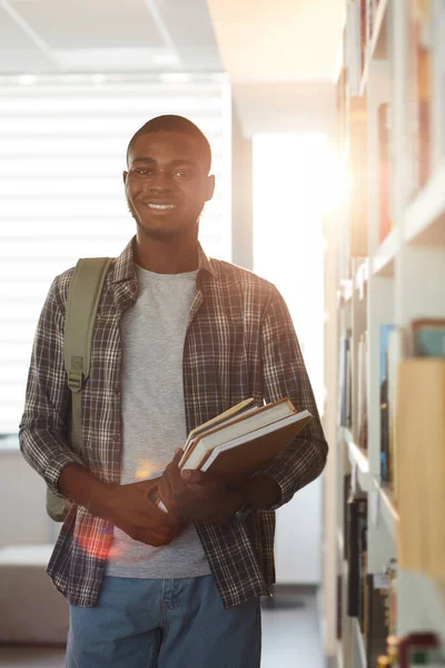 縦腰アップポートレートの若いですアフリカ系アメリカ人男性保持本と笑顔でカメラで立ちながら学校図書館 — ストック写真