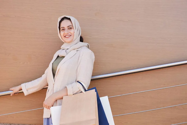在商场里 年轻的中东女人站在平整的背景下 拿着购物袋 对着相机微笑的画像 复制空间 — 图库照片