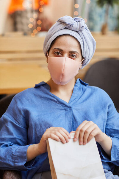 Vertical portrait of young Middle-Eastern woman wearing masks relaxing in cafe while enjoying shopping in mall, copy space