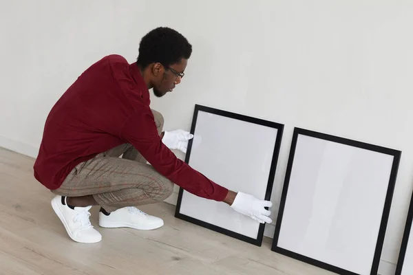 アフリカ系アメリカ人男性の高い角度のビューは アートギャラリーや展覧会 コピースペースを計画しながら床に空白の黒いフレームを設定します — ストック写真