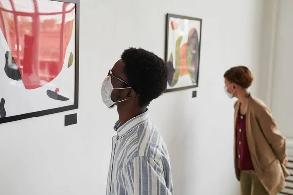 現代美術ギャラリーの展覧会でマスクをしながら絵画を見ている2人の若者の肖像画 コピースペース — ストック写真