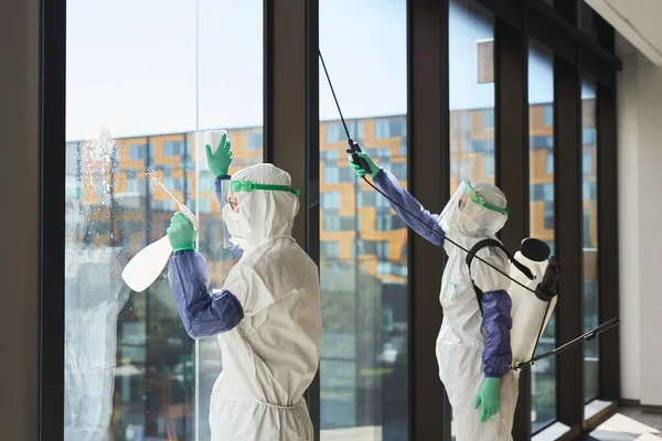 Potret Dua Pekerja Yang Mengenakan Pakaian Hazmat Mendisinfeksi Jendela Kantor — Stok Foto