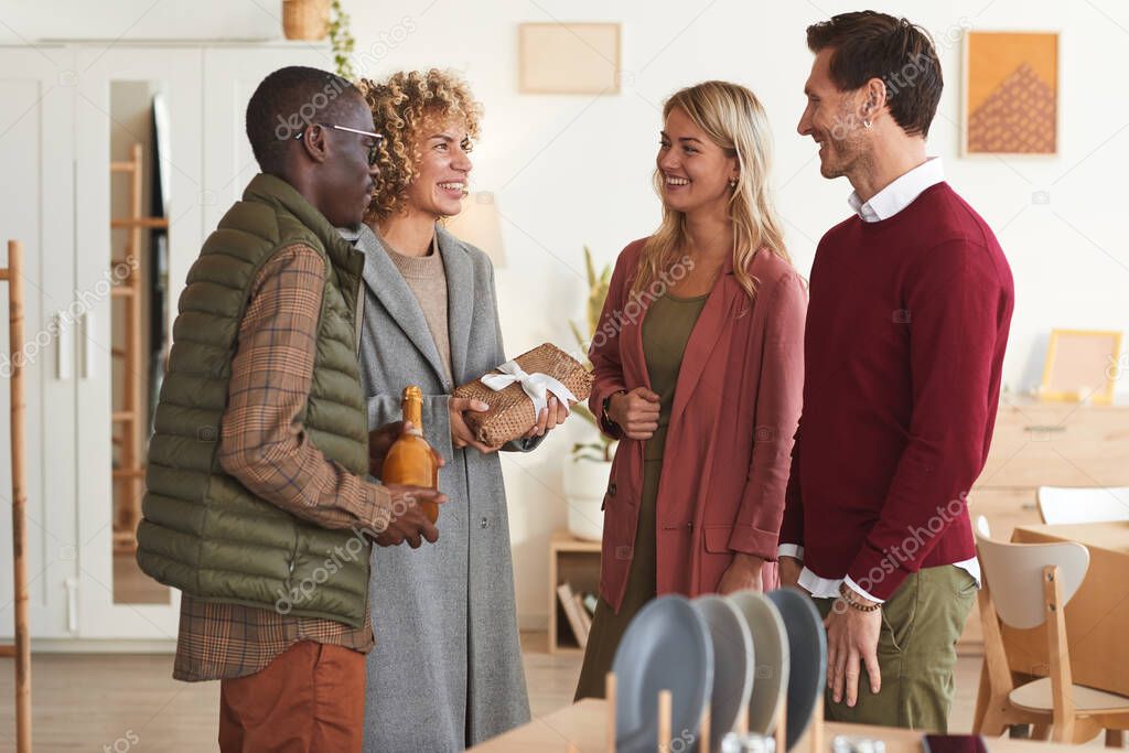 Multi-ethnic group of elegant adult people greeting each other and exchanging gifts while welcoming guests at dinner party indoors