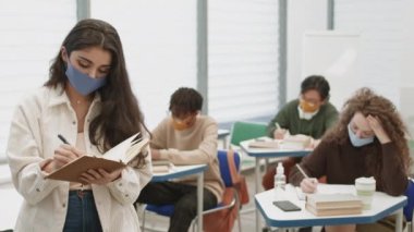 Orta karar, genç melez bir kadının çalışma kitabına notlar aldığı, sonra kapattığı ve kameraya baktığı, öğrencilerin önünde durduğu, sınıfta yazı yazdığı bir pov. Maske takan insanlar