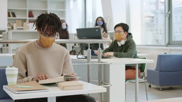 那些戴着黄布面罩和眼镜的非洲年轻人 一个接一个书桌地在图书馆看书 亚洲人坐在电脑前 姑娘们走在后面 — 图库视频影像