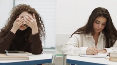 Göğüs göğüse gezen beyaz kadın makyaj yapıyor, melez kız not defterine yazıyor, Afrikalı adam sakız çiğniyor, Asyalı genç adam esniyor. Öğrenciler bir sırada sıraların başında oturuyor.