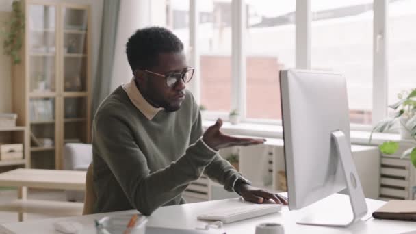 若いアフリカ系アメリカ人ビジネスマンの中には 職場で眼鏡をかけ コンピュータモニタを見て ビデオリンクで投資家と話をする姿が見られます — ストック動画