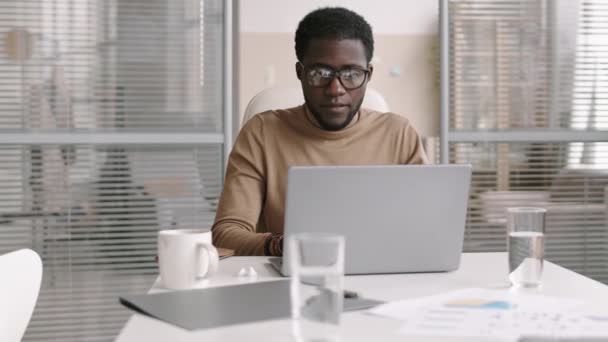 ラップトップの前にデスクトップに座ってビジネスパートナーとインターネットでコミュニケーションを取るアフリカ系アメリカ人ビジネスマンの追跡権 — ストック動画